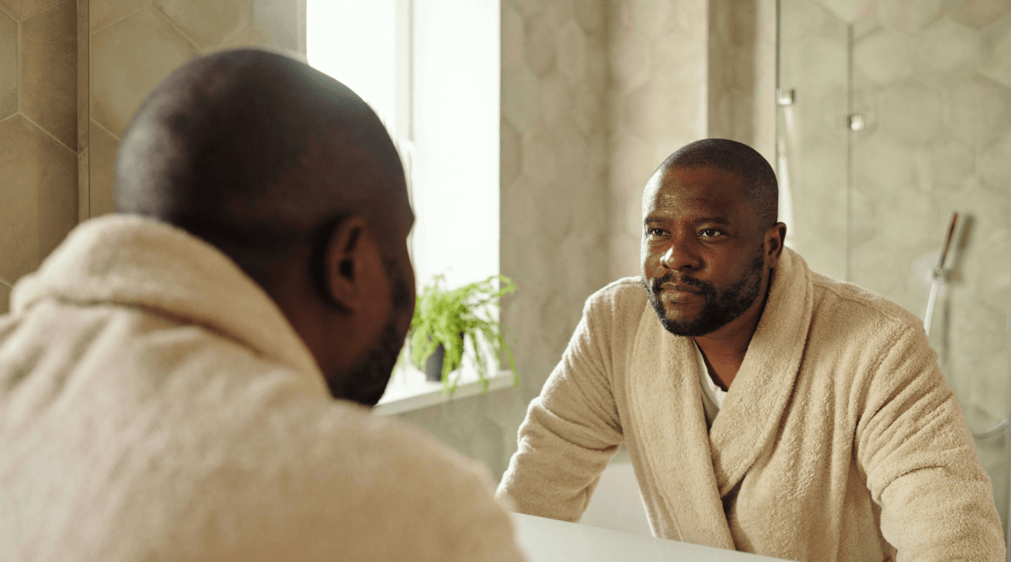 man in robe looking at reflection in bathroom mirror