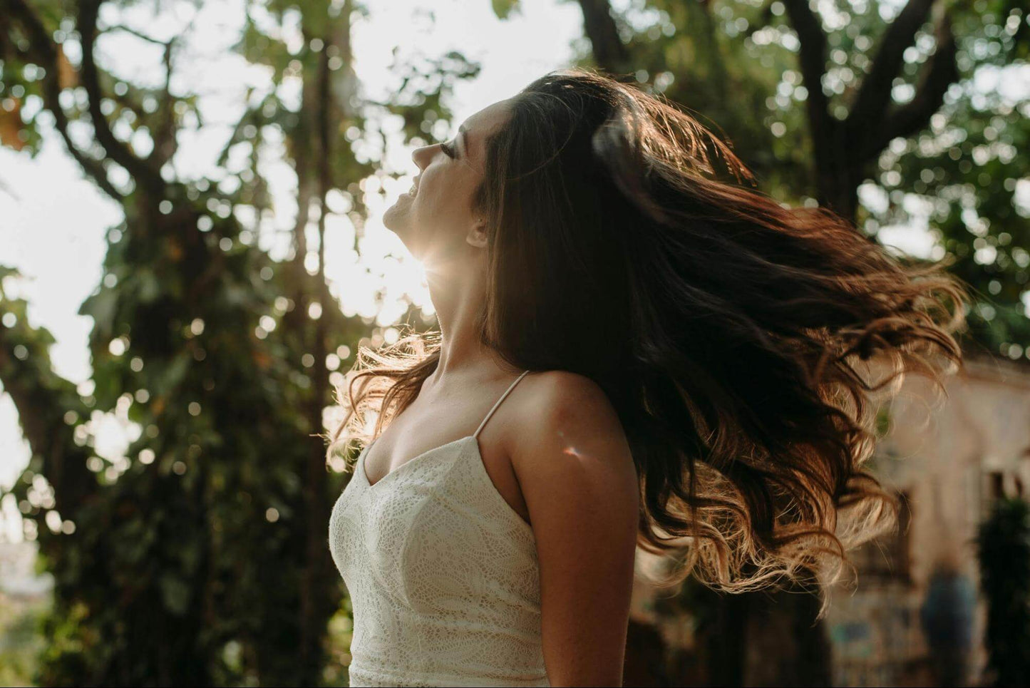 Woman in White Spaghetti Strap Dress with thick hair surrounded by trees