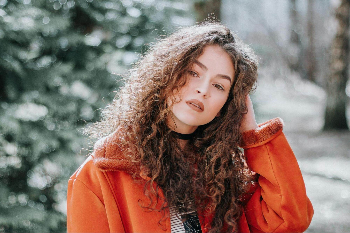 Woman in Orange Zip-up Jacket running hand through curly hair