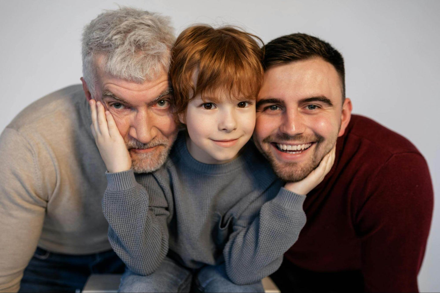 boy smiling with hands around the face of dad and grandpa